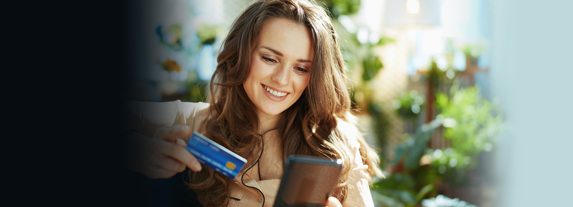 Chica Sentada Sosteniendo su Tarjeta de Crédito Mientras Compra en su Teléfono