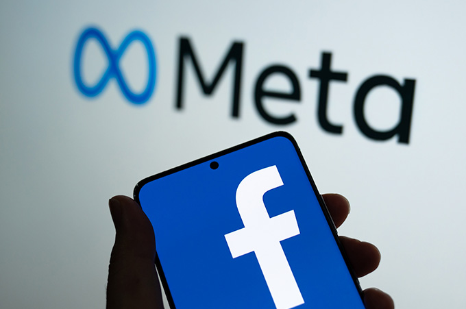 Mano Sosteniendo Smartphone con el Logo de Facebook y Logo de Metaverso Detrás
