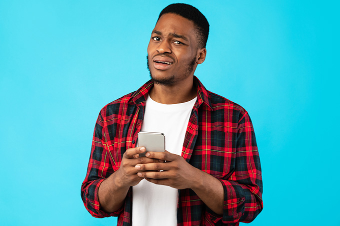 Hombre Joven con Smartphone en sus Manos y Gesto de Desagrado en su Rostro