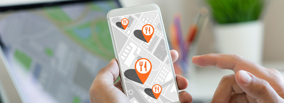 Manos Sosteniendo Smartphone con Mapa Digital e Iconos de Restaurantes que Muestran su Ubicación