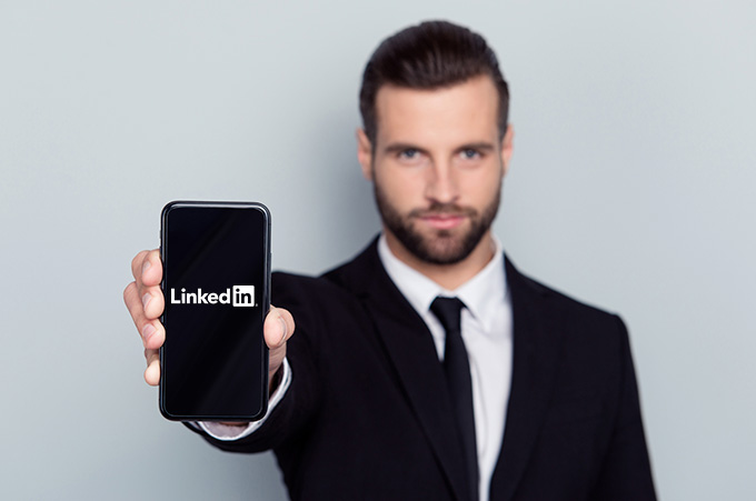 Empresario Mostrando Smartphone a la Cámara con Logo de LinkedIn en Pantalla
