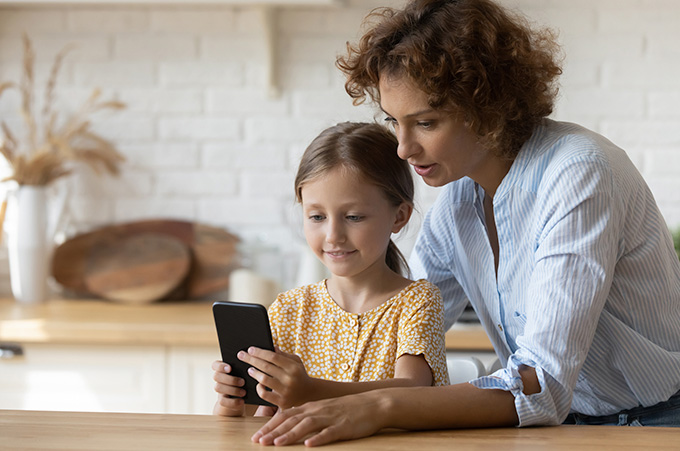 Madre Supervisando a Hija Mientras Navega en Redes Sociales con su Smartphone